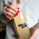 Hände mit rotlackierten Fingernägeln halten eine Flasche Wasserkefir